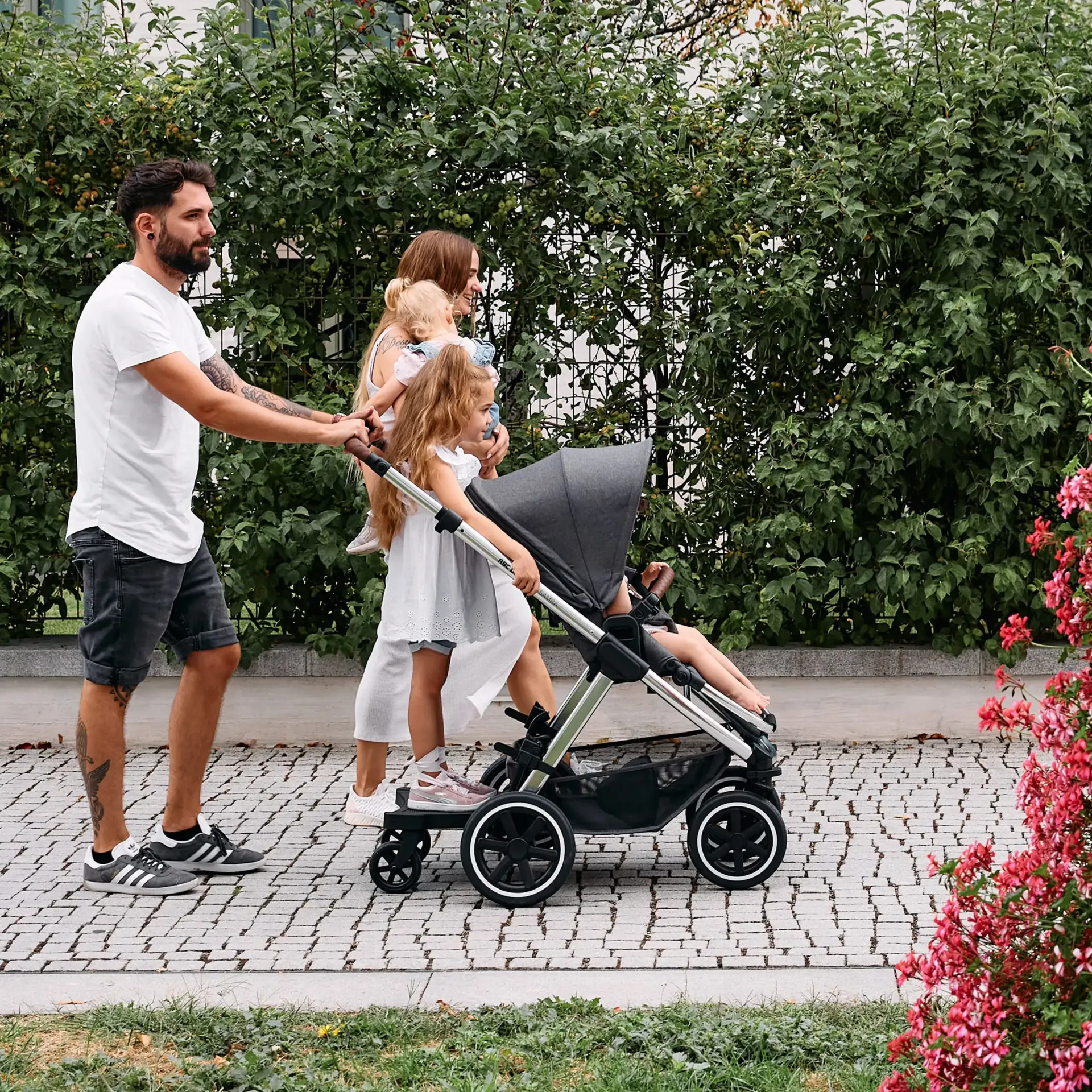 mann schiebt zwei kinder eins im buggy und eins auf dem montierten trittbett