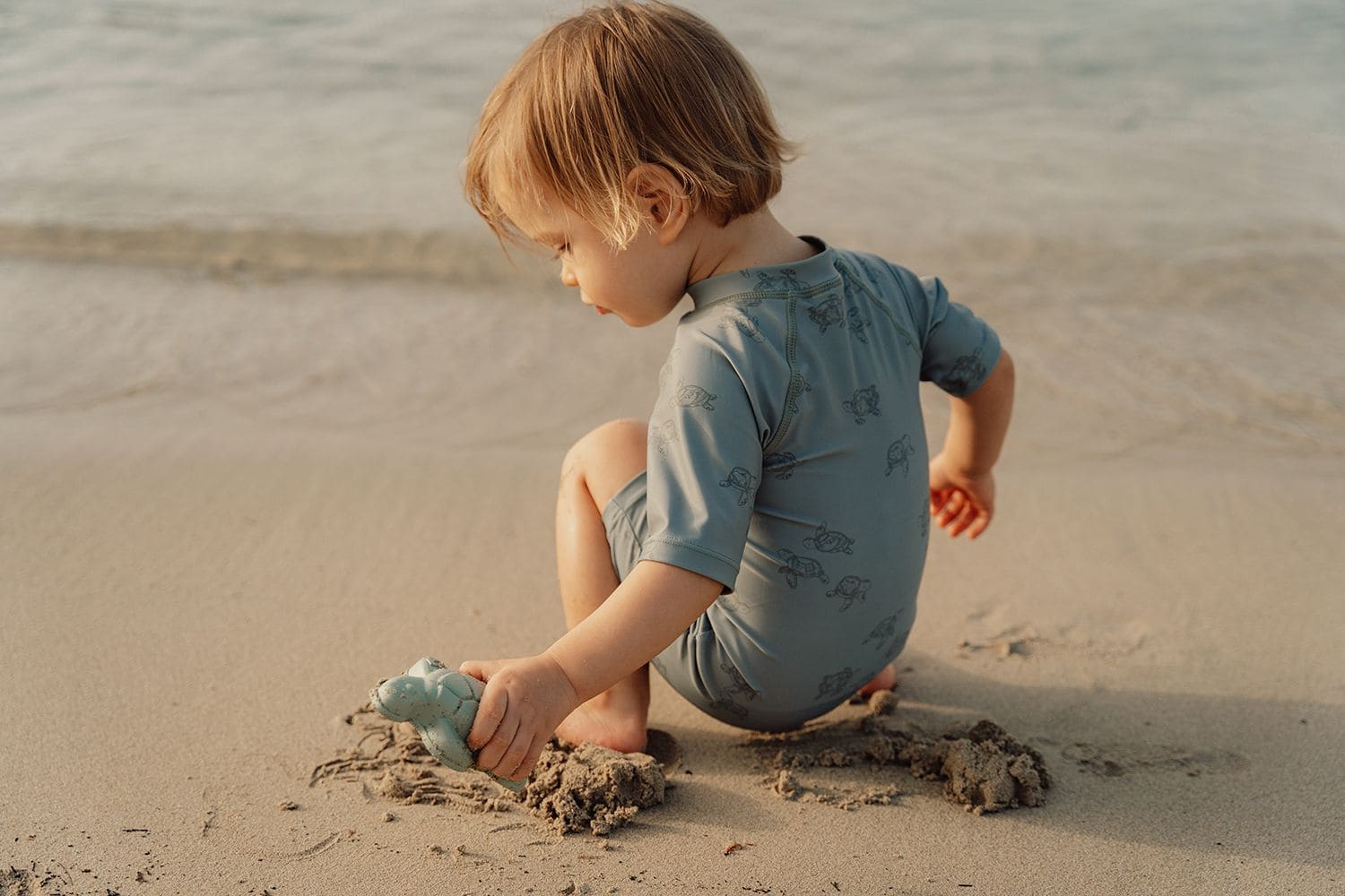 kind spielt mit förmchen am wasser